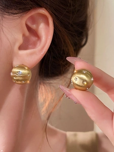 Detailed view of 18k gold plated ball earrings with brushed texture and star-shaped zircon