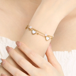 Close-up of gold double-layer bracelet featuring white pearls and heart charms on wrist