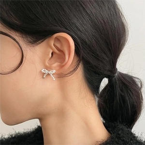 Detail of bow-shaped earring with pearl embellishment worn on a model ear