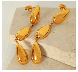 Macro shot of tiered gold teardrop earrings on a minimalist stone textured background