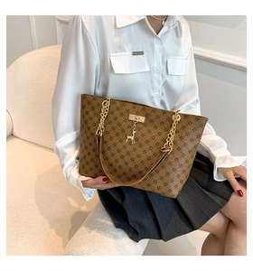 Close-up of brown patterned tote bag featuring gold chain strap and deer charm detail