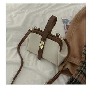 Detail of two-tone beige and brown leather handbag with gold clasp on a fabric background