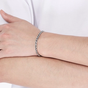 Detailed view of a silver wheat chain link bracelet worn on wrist over white fabric