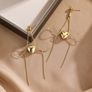 Macro view of gold snake chain bow earrings with heart pendants on satin cloth