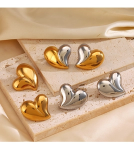 Tre paia di orecchini a cuore in metallo oro e argento su sfondo di pietra e seta fine