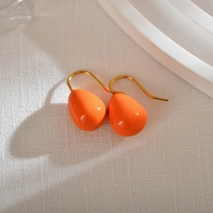 Detail of vibrant orange teardrop earrings with golden hooks on white textured background