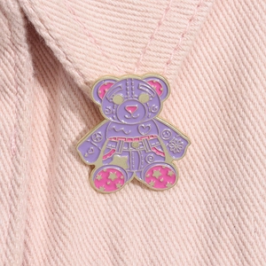 Macro detail of a purple and pink cartoon bear enamel brooch pinned on pink denim fabric