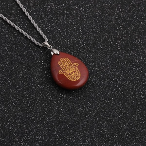 Macro detail of red stone Hamsa pendant with golden Evil Eye on silver rope chain