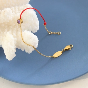 Red woven string bracelet with gold chain and purple gemstone on coral display