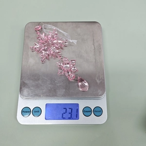 Pink acrylic snowflake ornament with a water drop pendant being weighed on a scale