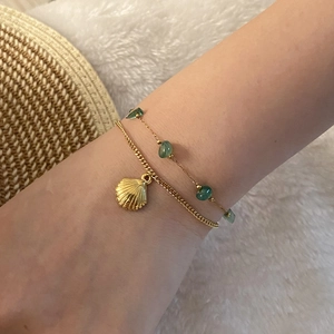 Close-up of golden shell charm bracelet and green natural stone beads on a woman's wrist