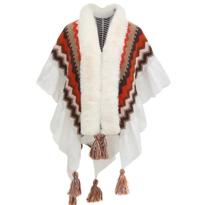 Detail of white knit poncho featuring a fur collar and multi-color herringbone patterns