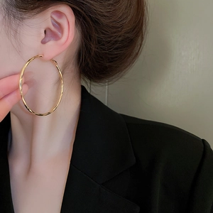 Detailed view of large gold twisted hoop earrings worn by a model in a black suit