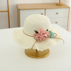 Detail of woven straw hat with lace brim and soft fabric floral accents on gold stand
