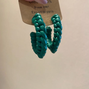 Detail of green leather woven C-shape hoop earring on a copper display card
