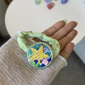Close-up of a light green fabric hair tie with a blue resin seashell and starfish pendant