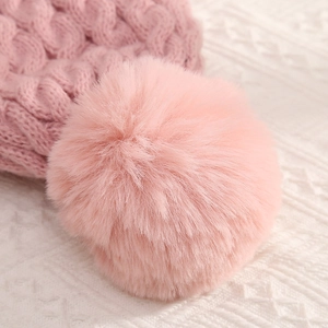 Pink knitted beanie hat featuring a fluffy faux fur pompom on a soft fabric background