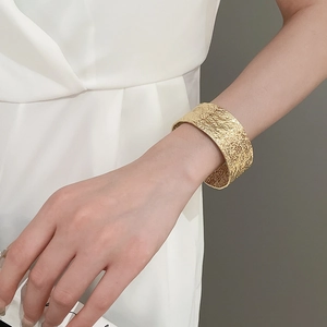 Detailed view of a wide gold cuff bracelet featuring a textured hammered metal surface