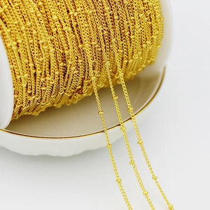 Macro shot of 18K gold-plated beaded chain on a spool showing texture and shine