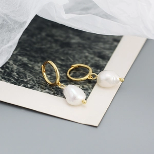 Detailed shot of golden hoop earrings featuring irregular white Baroque pearl pendants