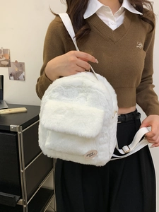 Mini mochila de felpa blanca con bordado llevada por una modelo sobre un suéter marrón