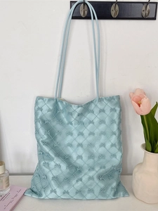 Light blue quilted shoulder tote bag with bow-knot embossed texture hanging on a wall hook