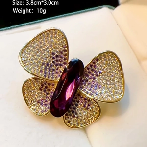 Elegant gold butterfly brooch with purple crystals and faceted gemstone on beige fabric