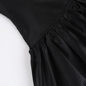 Detail of ruched waist stitching and glossy black fabric on a slim A-line dress
