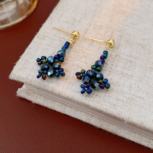 Macro detail of diamond-shaped floral beaded stud earrings on a linen texture book