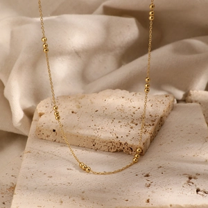 Minimalist 925 sterling silver gold beaded necklace on a textured stone background