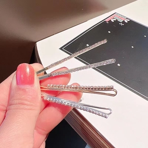 Close-up of four thin rhinestone-encrusted bobby pins with gold and silver metal bases