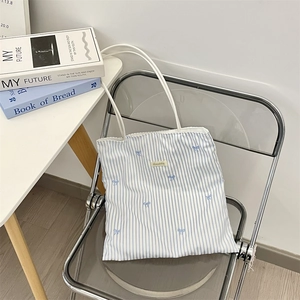Detail of blue striped canvas tote bag featuring delicate blue bow embroidery