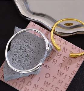 Makroaufnahme von minimalistischen gold- und silbernen Tropfenarmreifen auf grauem Stein