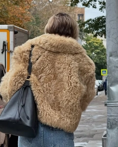 Femme en veste bouclée camel et sac seau en cuir noir lors d'une séance photo en extérieur
