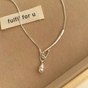 Detail of silver box chain with a white freshwater pearl pendant on a beige fabric base