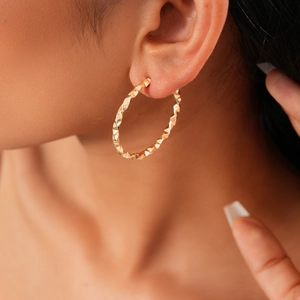 Close-up of geometric twisted C-shape gold earring on model showing metallic luster