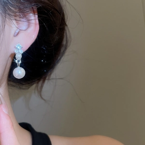 Close-up of silver diamond earrings with pearls worn by a model for a vintage elegant look