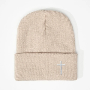 Detailed view of white cross embroidery on a beige knitted beanie with folded brim