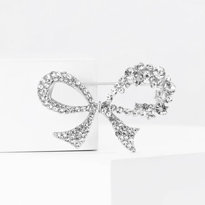 Elegant silver bow brooch with sparkling rhinestones on a minimalist white background