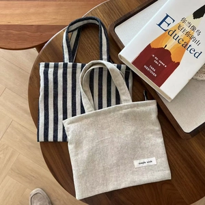 Detail view of striped and beige canvas tote bags on a rustic wooden table setup