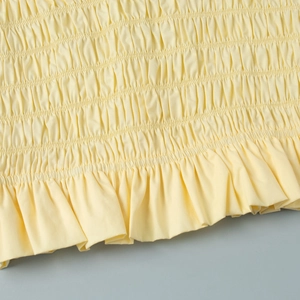 Detailed close-up of yellow smocked fabric with delicate ruffle hem and elastic texture