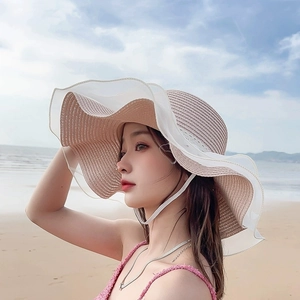 Detail of straw sun hat with white organza wavy lace trim on beach background