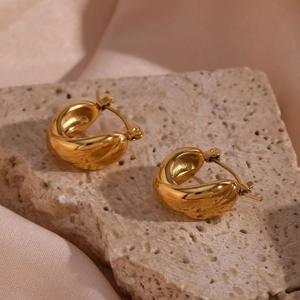 Detail of twisted gold earrings on beige silk and stone tray with elegant lighting