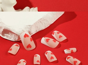 Detail of matte pink press-on nails with white French tips and red heart patterns
