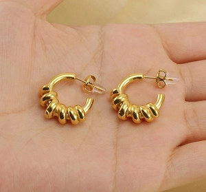 Nahaufnahme der goldenen C-Ohrringe mit Spiralstruktur und Schmetterlingsverschluss