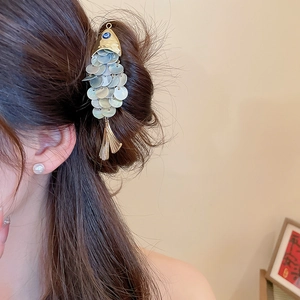 Detailed fish-shaped hair clip with shell scales and gold tassels on a low bun