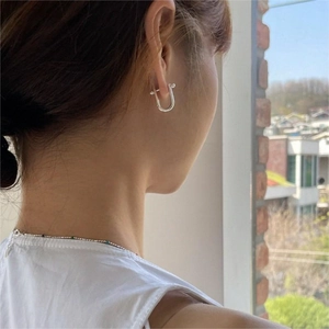 Detail of silver U-shaped earring worn on ear showing minimalist horseshoe metal design