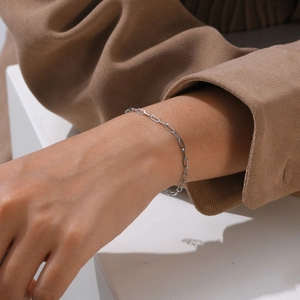 Close-up of polished silver paperclip chain bracelet worn on a velvet textured sleeve