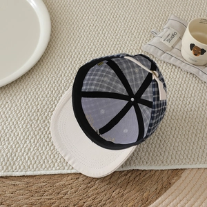 Detailed interior of checkered baseball cap showing reinforced black tapes and silver top button