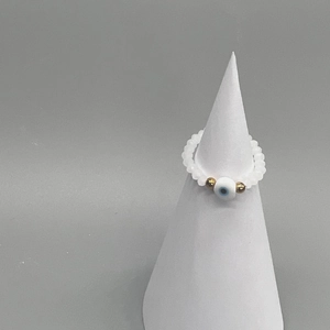 Detailed macro view of white bead stretch ring with blue evil eye charm on display stand